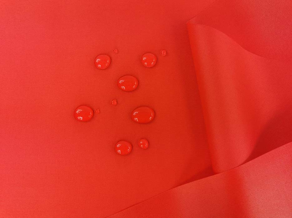 Zdjęcie prezentujące tkaninę wodoodporną w kolorze czerwonym z widocznymi kroplami wody nie wsiąkającymi w materiał