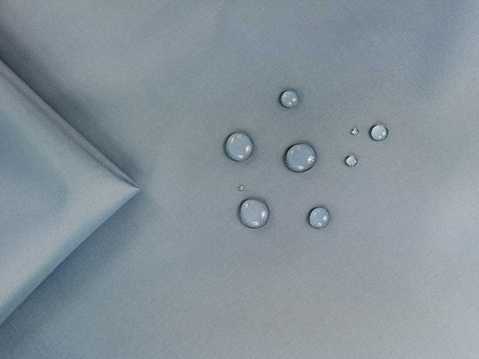 Zdjęcie prezentujące tkaninę wodoodporną w kolorze niebiesko-szarym z widocznymi kroplami wody na powierzchni materiału