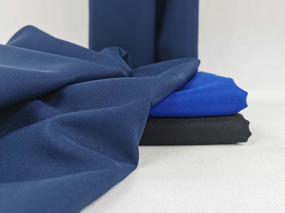 Zdjęcie przedstawiające tkaninę poliestrową Diagonal w kolorze granatowym ułożoną na materiale w kolorze niebieskim i czarnym