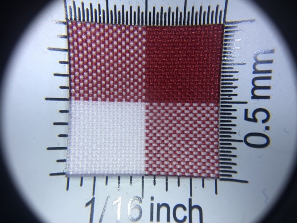 Zdjęcie przedstawia art. MM43Y, tkanina poliestrowa (100% poliester, gramatura 160 g/m2, szerokość 150 cm) w kolorze czerwonym (nr. 3661), we wzorze 206, w przybliżeniu, pod lupą, ukazanie struktury tkaniny.