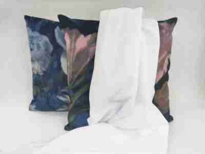 Zdjęcie prezentujące dzianinę drapaną poliestrową w kolorze białym na tle poduszek w kolorze granatowym z motywem kwiatów