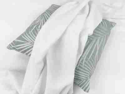 Zdjęcie przedstawiające białą dzianinę drapaną- materiał na poduszki i obicia mebli- na tle poduszki z motywem roślinnym
