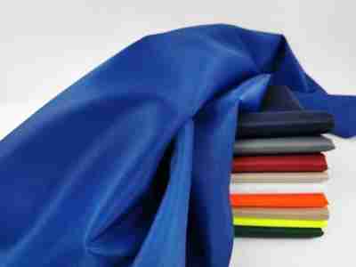 zdjęcie prezentujące niebieską Elanobawełnę Biver, wna tle materiałów w kolorze granatowym, szarym, czerwonym, beżowym, białym, pomarańczowym, piaskowym, seledynowym oraz zieleni butelkowej