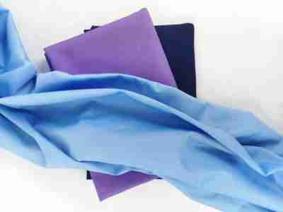 Zdjęcie prezentujące błękitną tkaninę Elanobawełnę Radus 1203 na tle materiałów w kolorze granatowym oraz fioletowym w odcieniu ciemnej lawendy