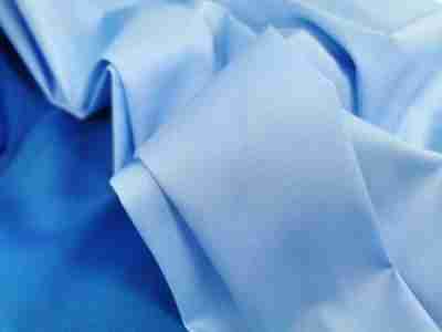 Zdjęcie przedstawiające przybliżenie na tkaninę Elanobawełnę Radus w kolorze jasnego błękitu na tle materiału w kolorze niebieskim