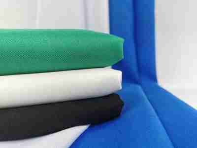 Zdjęcie przedstawiające tkaninę poliestrową Diagonal w kolorze jasnej zieleni, ecru i czerni na tle materiałów w kolorze białym i niebieskim