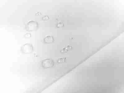 Zdjęcie przedstawiające białą tkaninę wodoodporną softshell SL19 w przybliżeniu na krople wody na powierzchni materiału