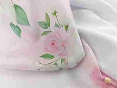 Zdjęcie prezentuje materiał Żorżeta- tkaninę na sukienki i dekoracje w kolorze białym i nadrukiem w róże w przybliżeniu