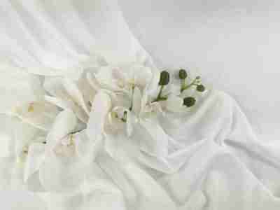 Zdjęcie przedstawiające białą poliestrową tkaninę Silki na tle kwiatu