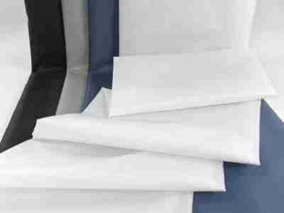 Zdjęcie przedstawiające białą tkaninę wodoodporną (Ortalion), materiał na kurtki i torby, na tle tkanin w kolorze czarnym, szarym i granatowym 