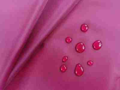 Zdjęcie prezentujące czerwoną tkaninę wodoodporną ortalion w przybliżeniu z kroplami wody na powierzchni materiału