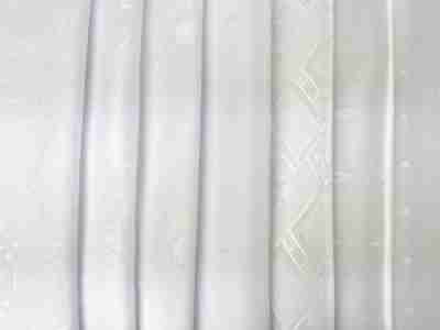 Zdjęcie prezentujące białe tkaniny obrusowe Żakard we wzorach świątecznych i codziennych