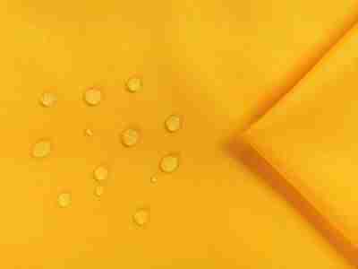 Zdjęcie prezentujące żółtą tkaninę wodoodporną Oxford S65N w przybliżeniu na krople wody na powierzchni materiału